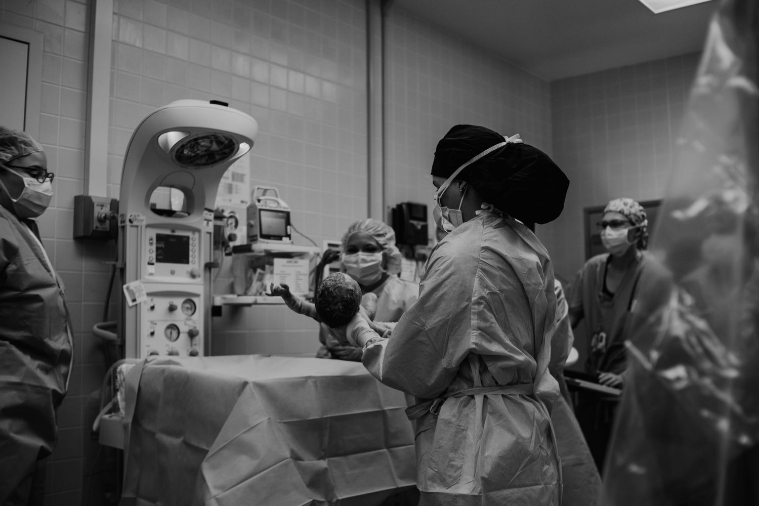 Black and white image of medical staff working in an operating room around surgical equipment and monitoring devices.