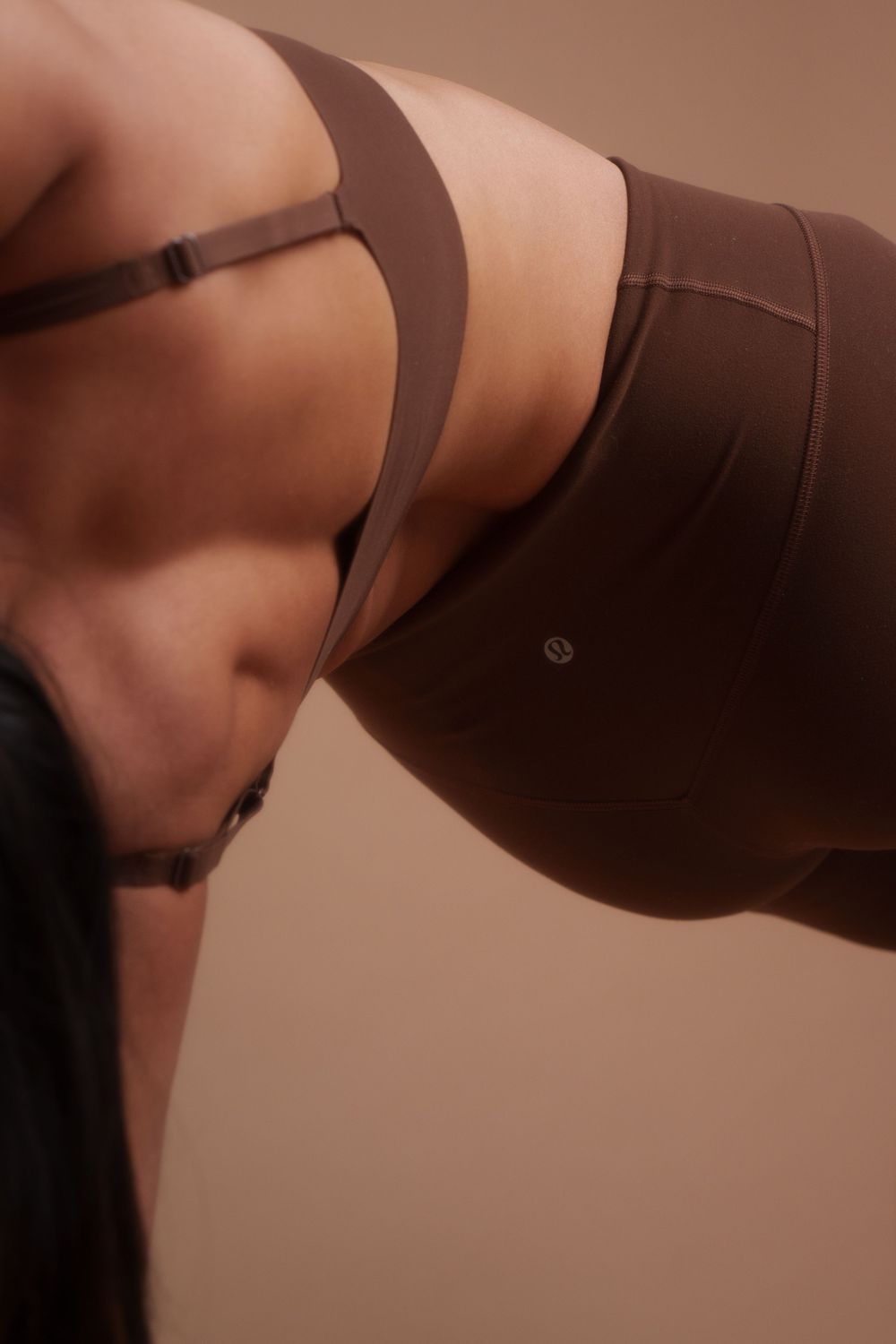 Close-up view of a brown sports bra and matching workout set against a neutral beige background.