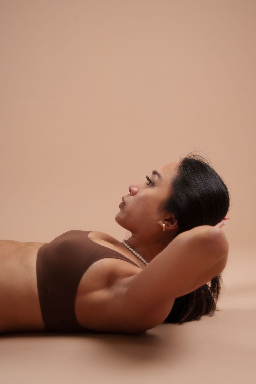 A model in athletic wear lies back against a neutral beige background in a serene wellness pose.