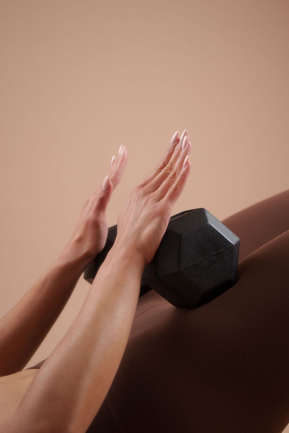 Two hands pushing away a black hexagonal dumbbell against a beige background in a minimalist fitness scene.
