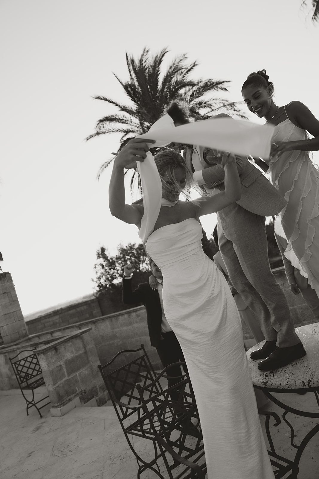 A black and white candid shot at an outdoor event shows people gathered on a patio with decorative railings.