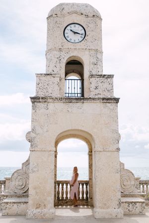 Historic white stone clock tower and archways of the Worth Avenue Clock Tower in Palm Beach, Florida against cloudy sky.