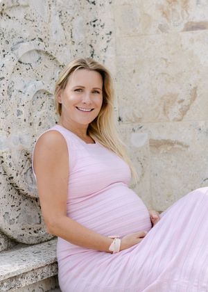 A person in a light pink dress poses against a textured stone wall in an artistic maternity photoshoot.