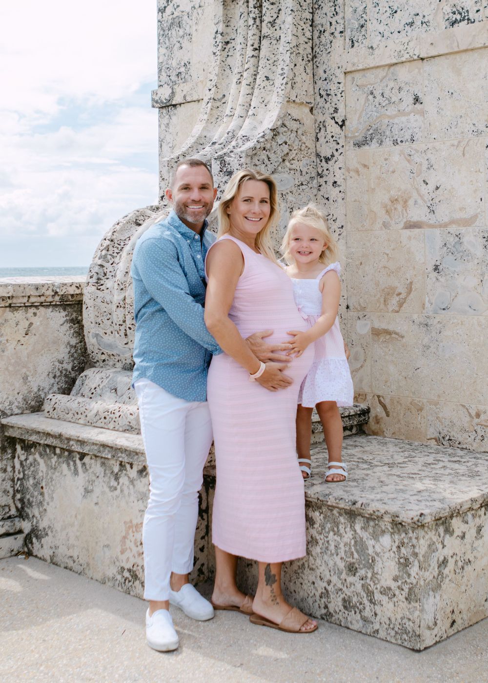 A family embraces together against a stone wall backdrop at a tropical location.