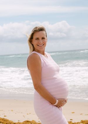A woman in a pink dress poses on a beach with ocean waves in the background.