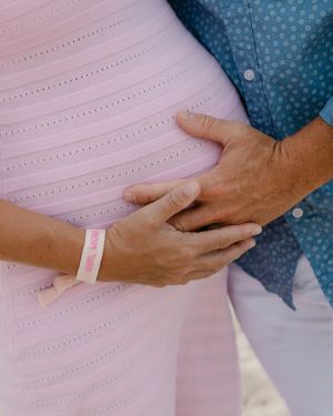 Close-up of hands gently resting on a pregnant belly wearing a pink dress with dotted pattern details.