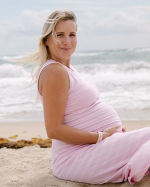A person in a soft pink dress reclines on a sandy beach with ocean waves in the background.