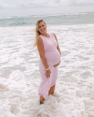 A woman in a pink dress stands in the ocean waves at the beach during a photo session.