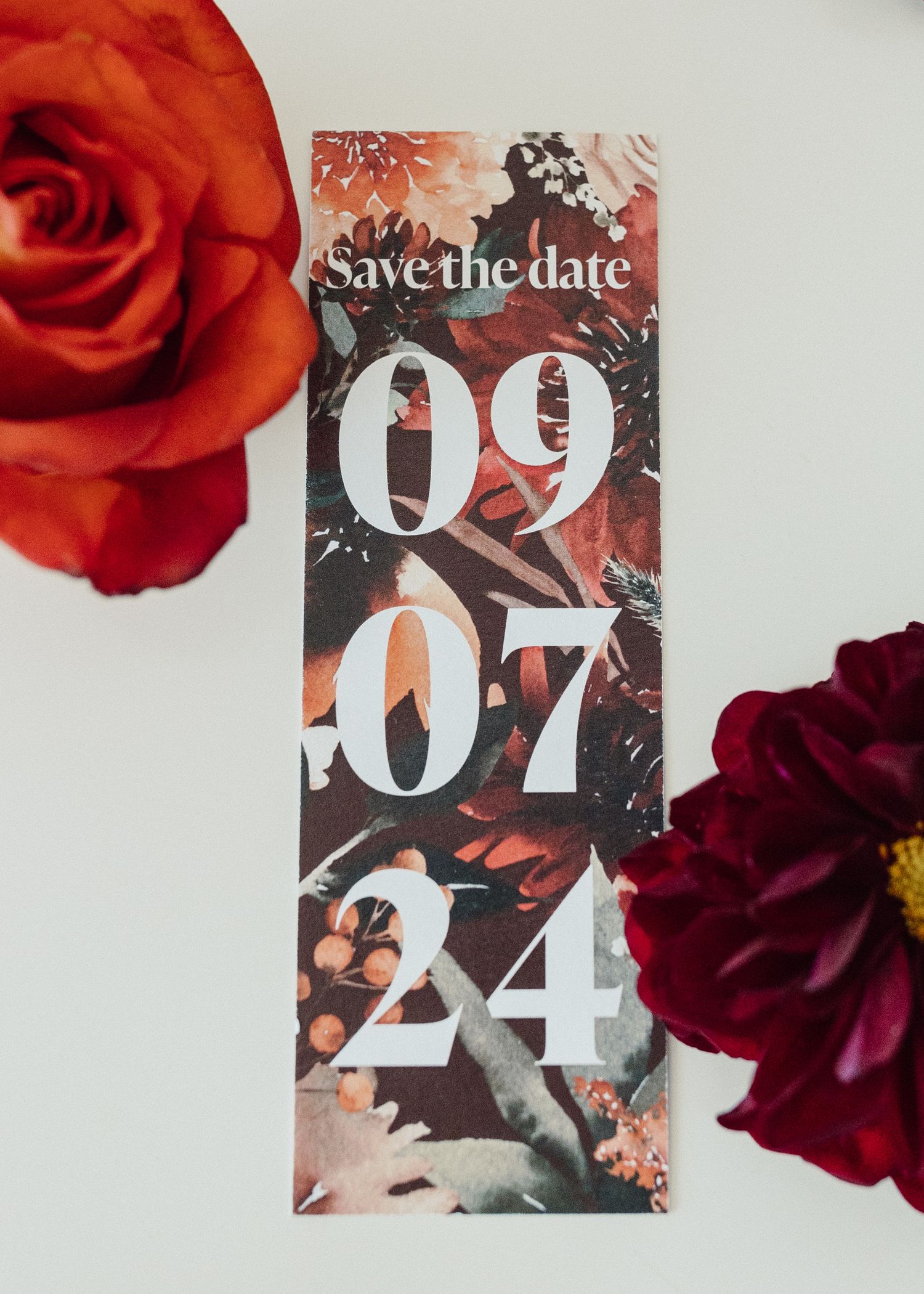Save the date card with bold typography surrounded by red and burgundy roses.