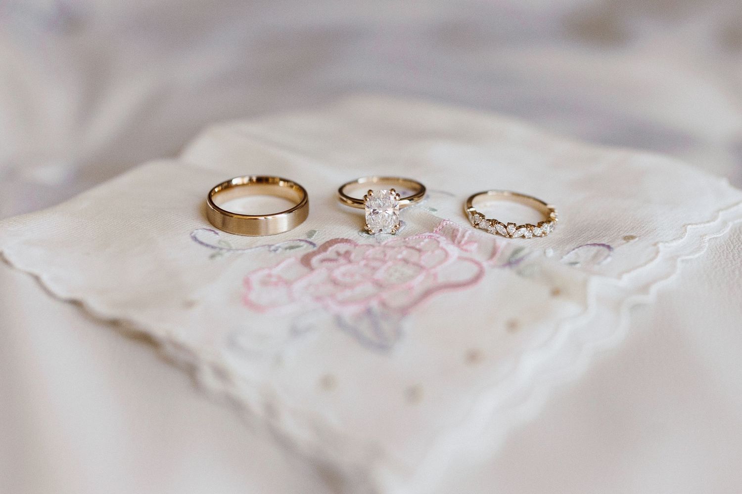 Wedding rings and jewelry arranged on delicate white lace fabric.