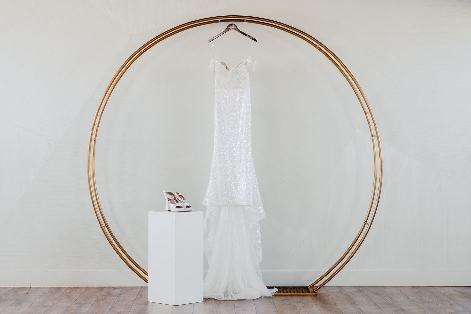 Modern wedding dress display with circular copper arch against white wall.
