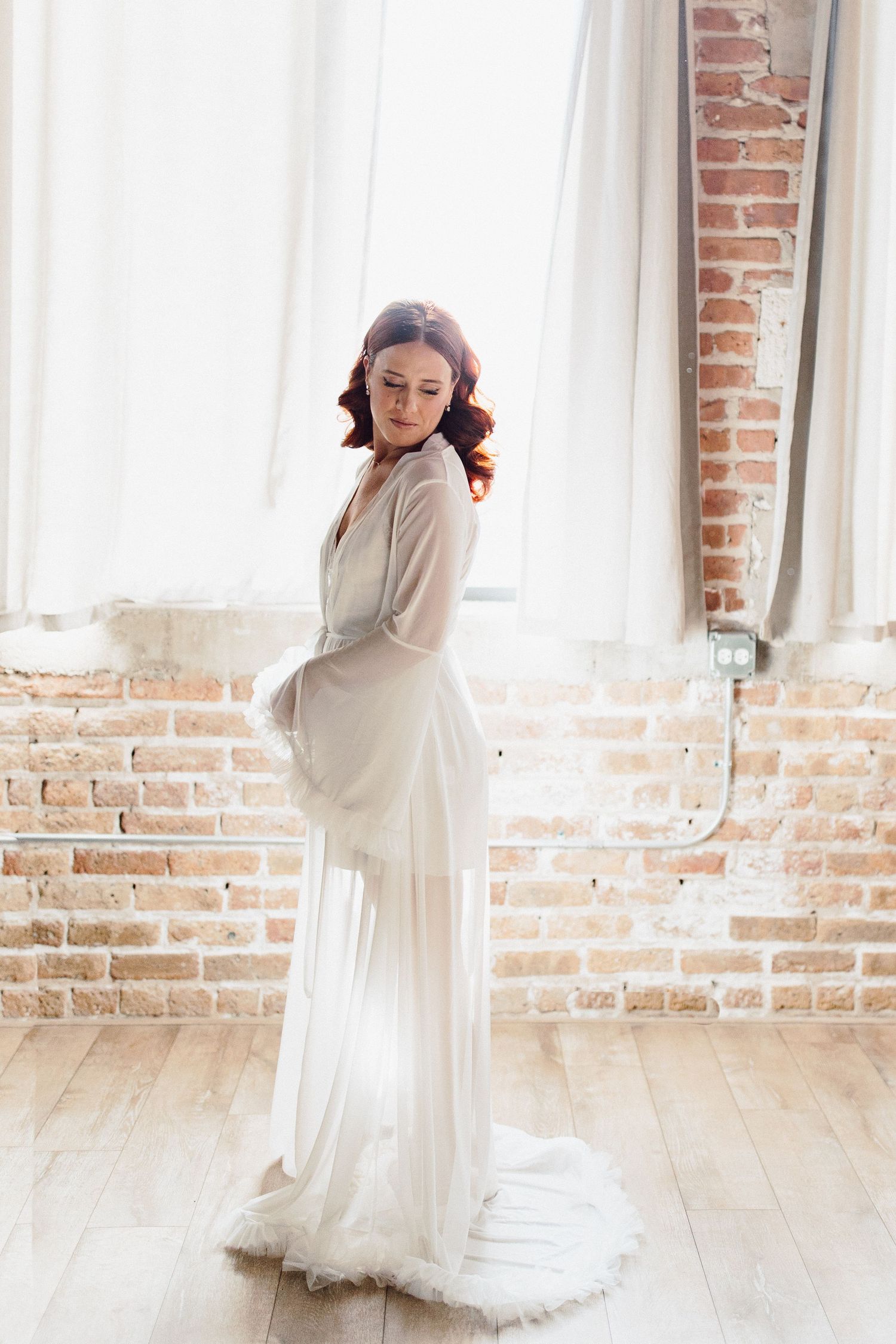 Romantic bridal portraits in white dress against exposed brick and natural window light.