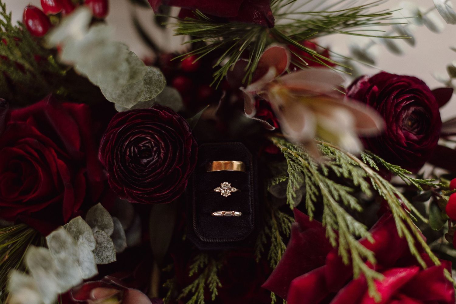 Deep red roses and greenery wedding floral arrangement with rings.