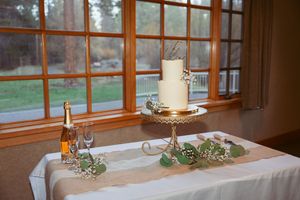 Elegant table setting with white candle on silver stand near window with bottle of wine and greenery accents.