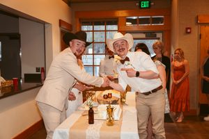 Two people in casual attire stand by a table with drinks and decorations at an indoor event venue.