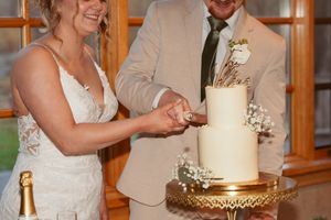 Newlyweds cutting their elegant white and gold wedding cake together at reception.