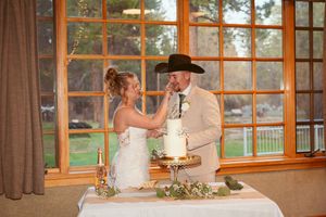 Couple cuts their wedding cake together in a rustic venue with large windows.
