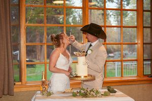Wedding cake cutting moment captured in a venue with large windows overlooking nature.