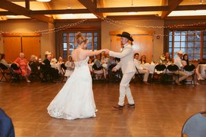 A couple dances together at a wedding reception in a rustic wood-beamed venue decorated with string lights.