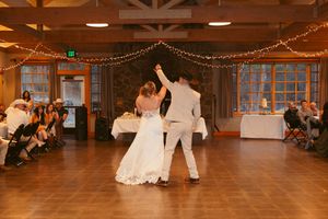 A couple performs an elegant dance move on a wooden dance floor beneath twinkling string lights at their indoor wedding reception.