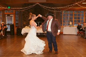 Couple dancing at a rustic wedding reception venue decorated with string lights on wooden walls and beams.