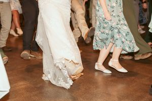 Wedding guests dancing with focus on flowing dresses and feet on rustic dance floor.