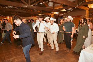 Wedding reception guests dancing in a rustic barn venue decorated with string lights overhead.