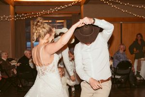 A joyful wedding couple dancing together under string lights at their reception celebration.