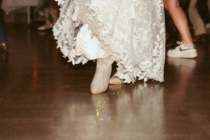 Close-up of white lace wedding dress hem and boots on wooden dance floor.