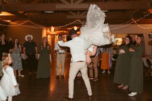 Wedding reception dance party with guests celebrating under string lights in an indoor venue.