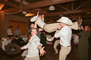 People dancing and celebrating at an indoor reception with string lights and rustic decor.