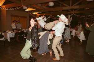 Wedding guests dance energetically on rustic wood floor under string lights at reception.