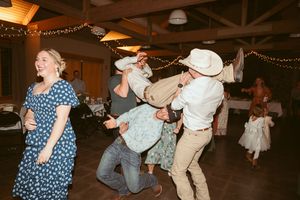 A lively dance party scene at a rustic reception venue with string lights and cowboy hats.