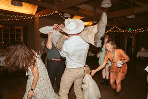 Lively wedding reception dance party scene with cowboy hats and string lights.