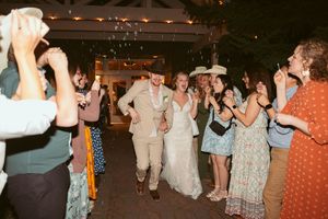 Wedding celebration as newlyweds walk through a crowd of guests during their reception at a dimly lit venue.