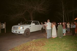 Wedding guests line up alongside a white pickup truck at night during the couple's departure.