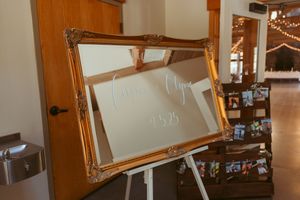 Ornate gold vintage mirror frame displayed on an easel at a wedding reception venue.