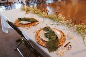 Elegant table setting with wicker charger plates, sage green napkins, and delicate baby's breath garland on white tablecloth.