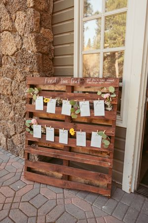 Rustic wooden pallet seating chart display decorated with florals and paper cards.