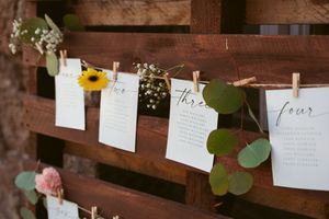 Wedding stationery and greenery hanging on a rustic wooden wall with clothespins and delicate floral accents.