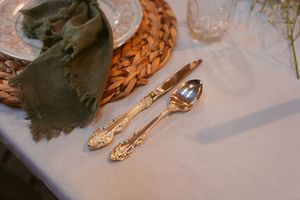 Elegant vintage silverware and napkin arranged on white tablecloth with woven placemat.