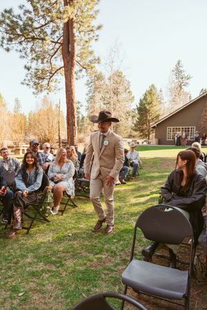 A western-themed outdoor wedding ceremony with guests seated on folding chairs among tall pine trees.