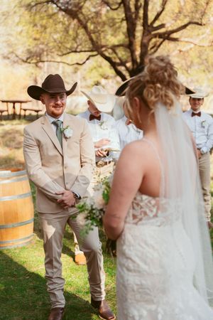 Rustic outdoor wedding ceremony with wine barrels and natural decor under a large tree.