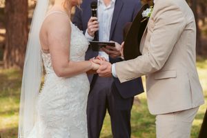 A wedding ceremony in progress showing a couple holding hands with an officiant in navy blue.