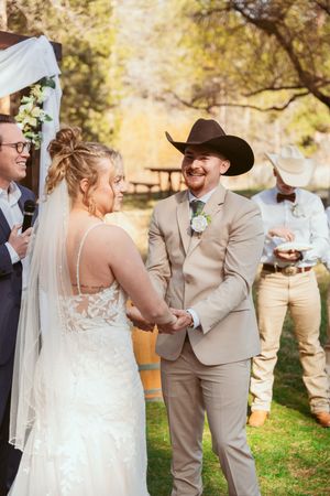 Outdoor wedding ceremony under white arch with couple in western-themed attire.