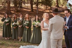 Outdoor forest wedding ceremony with bridesmaids in long sage green dresses standing in a line beside the couple.