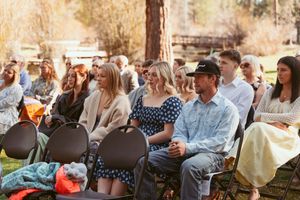 Wedding guests seated on folding chairs at outdoor forest ceremony.