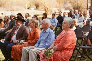 Wedding guests in formal attire seated outdoors with seniors in coral and blue clothing.