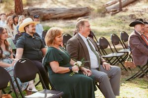 Wedding attendees in western attire watching ceremony from folding chairs in forest setting.