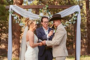 Outdoor wedding ceremony under a draped arch with florals in a rustic forest setting.